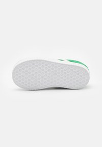 White rubber sneaker sole with a textured grip pattern; features green accents on the sides and a smooth fabric upper.