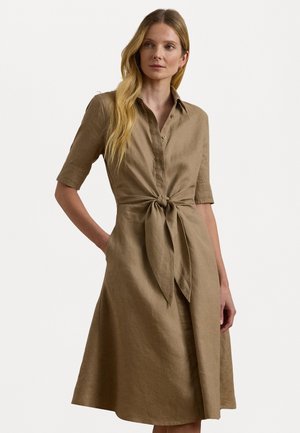 Brown linen dress with short sleeves, button-down front, tie waist detail, and flowing skirt. Smooth texture and natural finish.