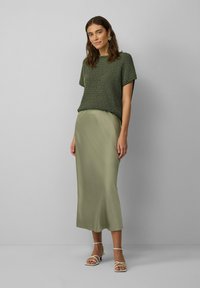 Top en tricot vert à manches courtes, associé à une jupe en satin vert clair lisse. Des sandales à brides transparentes complètent la tenue. Design simple.