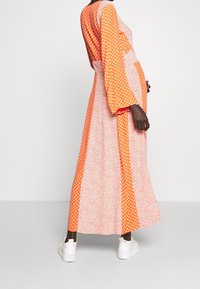 Robe longue à manches longues en orange à pois blancs, avec un motif floral contrastant, fabriquée en tissu léger.