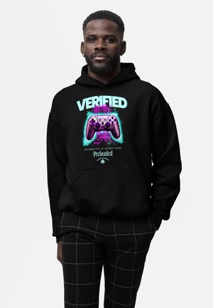 Mężczyzna w czarnej bluzie z kapturem z neonowym motywem kontrolera do gier i napisem "Verified Gamer", w połączeniu z czarnymi spodnimi w kratkę.