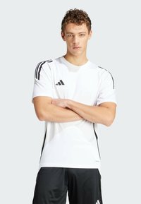 T-shirt de sport blanc avec des accents noirs sur les épaules et les côtés. Fabriqué en matériau léger. Présente le logo Adidas sur la poitrine.