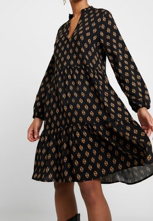 Černé šaty s dlouhými rukávy, výstřihem do V a nařasenou vrstvenou sukní. Mají květinový motiv ve zlatých a hnědých odstínech.