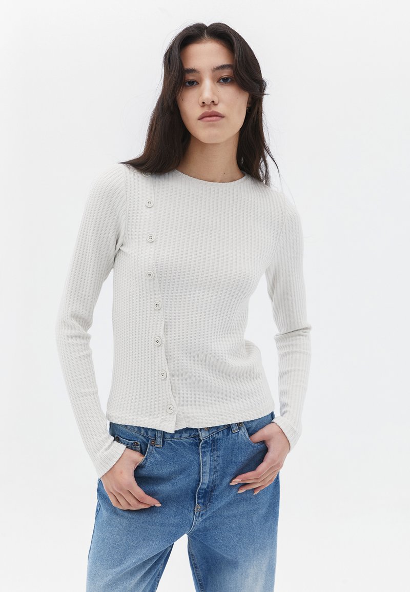 Maglione a maniche lunghe grigio chiaro a costine con scollatura rotonda e dettagli con bottoni su un lato. Abbinato a jeans in denim blu larghi.