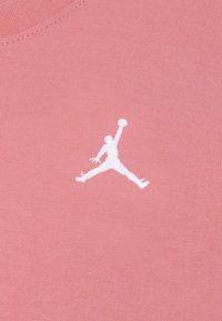Roza majica od tkanine s bijelim izvezenim Jumpman logotipom na lijevom prsnom dijelu. Glatka tekstura s okruglim izrezom.