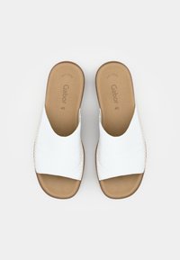 Bílé kožené skládací sandály s širokými popruhy a hnědou polstrovanou stélkou. Obsahují béžové prošívání a minimalistický design, vhodné pro neformální nošení.