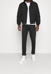 Svart bomberjacka med huva, två framfickor, kombinerad med mörka jeans och vita sneakers. Enkelt, funktionellt design.
