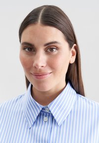 Camicia azzurra a righe, con colletto a punta, caratterizzata da strisce verticali bianche e una texture di tessuto morbida.