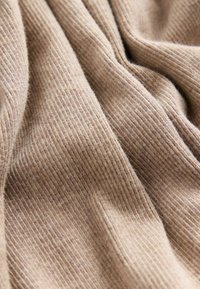 Tessuto a coste beige morbido con pieghe delicate che mostrano la texture e i dettagli di maglia fine in vista ravvicinata.