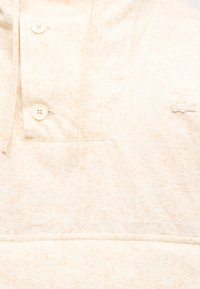 Ανοιχτό μπεζ πουλόβερ με υφαντό μοτίβο, διακοσμημένο με δύο κουμπιά στον λαιμό και μικρό κεντητό λογότυπο στο στήθος.