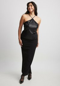 Svart paljett-top med justerbara korsettsnören, i kombination med en figurnära svart kjol. Mot en neutral bakgrund.