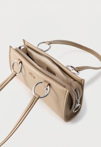 Μπεζ δερμάτινη τσάντα χειρός με ασημένιους κυκλικούς μεταλλικούς κρίκους, δύο θήκες με φερμουάρ και αποσπώμενο ιμάντα ώμου σε λευκό φόντο.