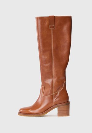 Bota castanha de couro até ao joelho, com bico quadrado, pespontos contrastantes, detalhe de faixa nas costas e um salto bloco de madeira moderado.