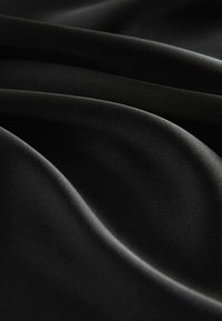 Tissu en satin noir drapé et plié, mettant en valeur une texture lisse et un éclat subtil. Le matériau semble luxueux et doux.