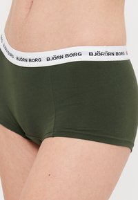 Boxer shorts in cotone verde scuro con una cintura elastica bianca che presenta il testo "BJÖRN BORG" in nero. Tessuto liscio e design aderente.