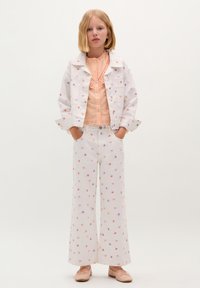 Witte denimjack en wijde broek met multicolore bloemenprint. Perzikkleurige blouse met kantdetails. Zachtroze balletschoenen.