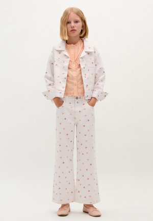 Veste en denim blanche et pantalons larges avec des imprimés floraux multicolores. Blouse pêche avec des détails en dentelle. Ballerines roses pâles.