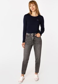 Granatowa koszula z długim rękawem i okrągłym dekoltem, zestawiona z szarymi, wysokim stanem dżinsami i białymi trampkami z czerwonymi akcentami.