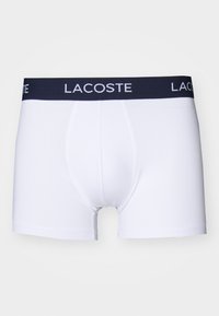 Fehér boxer alsónadrág, tengerészkék elasztikus derékkal, amelyen a Lacoste logó található. Sima tapintású, testhez álló fazon, nyitott sliccel.