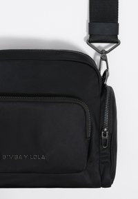 Must kollane nailonist õlakott siledast tekstuurist, millel on ees lukuga tasku ja reguleeritav rihm. Ees on deveeritud brändi logo.