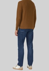 Bruin, gebreid shirt met lange mouwen gecombineerd met blauwe spijkerbroek. De spijkerbroek heeft twee achterzakken met lichtblauwe stiksels. Casual witte sneakers.