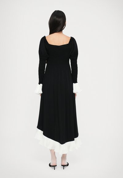 Rochie maxi neagră cu un corset plisat, mâneci bufante și tiv plisat alb. Purtați-o cu sandale negre cu toc.