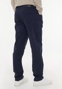 Navyblaue Hosen aus Baumwollmischgewebe, mit zwei Gesäßtaschen und einem strukturierten Taillenbund. Kombiniert mit weißen Sneakern.