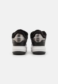 Ett par svarta och grå sneakers med vita sulor, pälsfoder runt öppningen och "KARL LAGERFELD"-logotyp på hälpartiet.