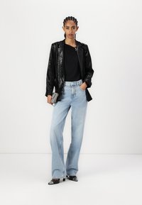 Čierny lesklý blejzer cez čierny top, skombinovaný so svetlo modrými širokými džínsmi. Modelka drží striebornú clutch kabelku a na nohách má čierne klasické topánky.