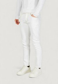 Vaqueros blancos con costuras doradas, corte ajustado y bolsillos laterales, combinados con zapatillas blancas de textura suave y diseño minimalista.