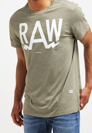 T-shirt manches courtes vert olive en coton doux, avec un grand logo blanc "RAW" aux accents angulaires sur le devant.