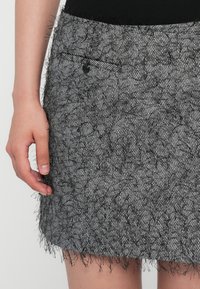Een zwart-wit houndstoothrok met franjes aan de onderrand, voorzien van een klein zijvak met een knoopsluiting.
