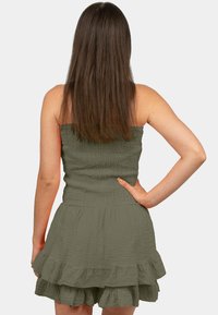 Olijfgroene strapless jurk met een gesmokte taille en gelaagde rufflezoom. Zacht, textuurstof en een getailleerde taille accentueren de vorm.