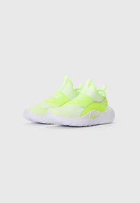 Une paire de baskets slip-on Nike de couleur jaune fluo et blanche avec des sangles élastiques et des semelles rembourrées sur un fond blanc uni.