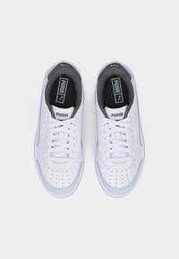 Ζευγάρι λευκών αθλητικών παπουτσιών Puma με μαύρες εσωτερικές σόλες, γκρι λεπτομέρειες και λευκά κορδόνια, σε θέα από πάνω πάνω σε απλό φόντο.