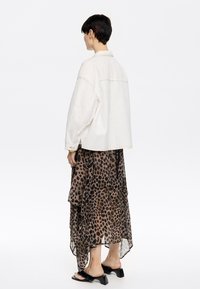 Veste en denim blanche surdimensionnée avec un empiècement au dos, associée à une jupe en couches en tulle à imprimé léopard, et des sandales noires à talons carrés.