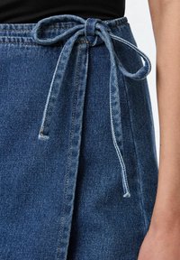 Denimhame, jossa on sininen sävy ja sidottu vyöyksikkö. Kangas on sileäpintaista ja siinä on rento, kiertävä malli.