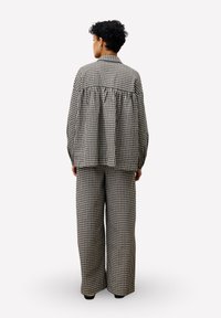 Persoon met kort, krullend haar in een bijpassend zwart-wit geblokt oversized shirt en wijde broek, gezien van achteren.