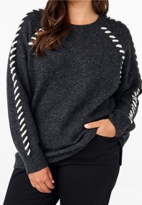 Flauschiger dunkelgrauer Pullover mit weißen Schnürdetails entlang der Ärmel und gerippten Bündchen. Hergestellt aus einem strukturierten Strickstoff und verfügt über eine lockere Passform.