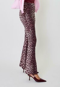 Hlače v leopardjem vzorcu, razširjene v barvah temno rdeče in roza, izdelane iz gladkega materiala, v kombinaciji z sijočimi temno rdečimi stiletnimi petami.