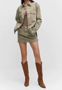 Khaki denim jack met twee borstzakken, gecombineerd met een bijpassende denim mini-jurk en bruine suede kniehoge laarzen met decoratieve stiksels.