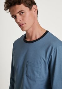 Langsleeve, blauwe katoenen t-shirt met een zwarte ronde hals en een borstzak. Zachte textuur met een losse pasvorm.