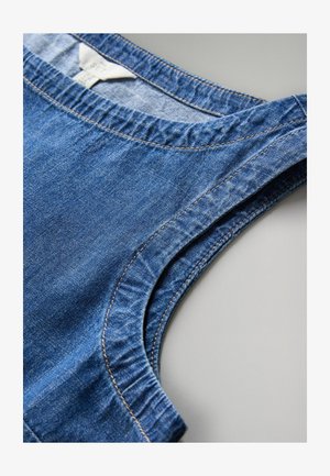 Blå denim ärmlös topp med rundad halsringning och synliga sömmar, lagd platt på en ljusgrå yta.