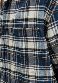 Rutet flannel skjorte i blå, sort og creme farver med en blød tekstur, knaplukning foran og en brystlomme.