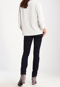Suéter blanco texturizado con mangas tres cuartos, combinado con jeans slim fit de color azul oscuro y botas de tacón alto gris hasta el tobillo.