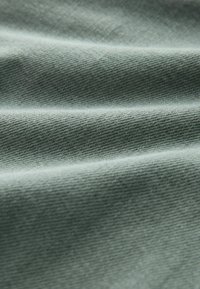 Groene katoenstof met een gladde structuur, die plooien en een subtiel weefpatroon vertoont. Licht weerkaatst zachtjes van het oppervlak.