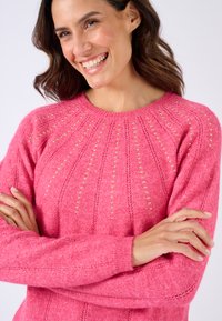 Maglione rosa a maglia con scollatura rotonda, modelli testurizzati e dettagli dorati lungo le spalle. Maniche lunghe e polsini a costine.