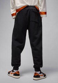 Zwarte joggingbroeken met een relaxte pasvorm, voorzien van een achterzak en geribde manchetten, gecombineerd met zwarte en oranje sneakers.