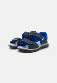 Schwarze und blaue Sandalen mit Klettverschlüssen, offener Zehenpartie, gepolsterten Innensohlen und strukturierten Gummisohlen für besseren Halt.