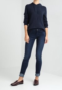 Marinblå huvtröja, mörka skinny jeans och bordeauxfärgade loafers. Jeansarna har uppvikta fållar; tröjan har en texturerad tyg och ribbade ärmar.